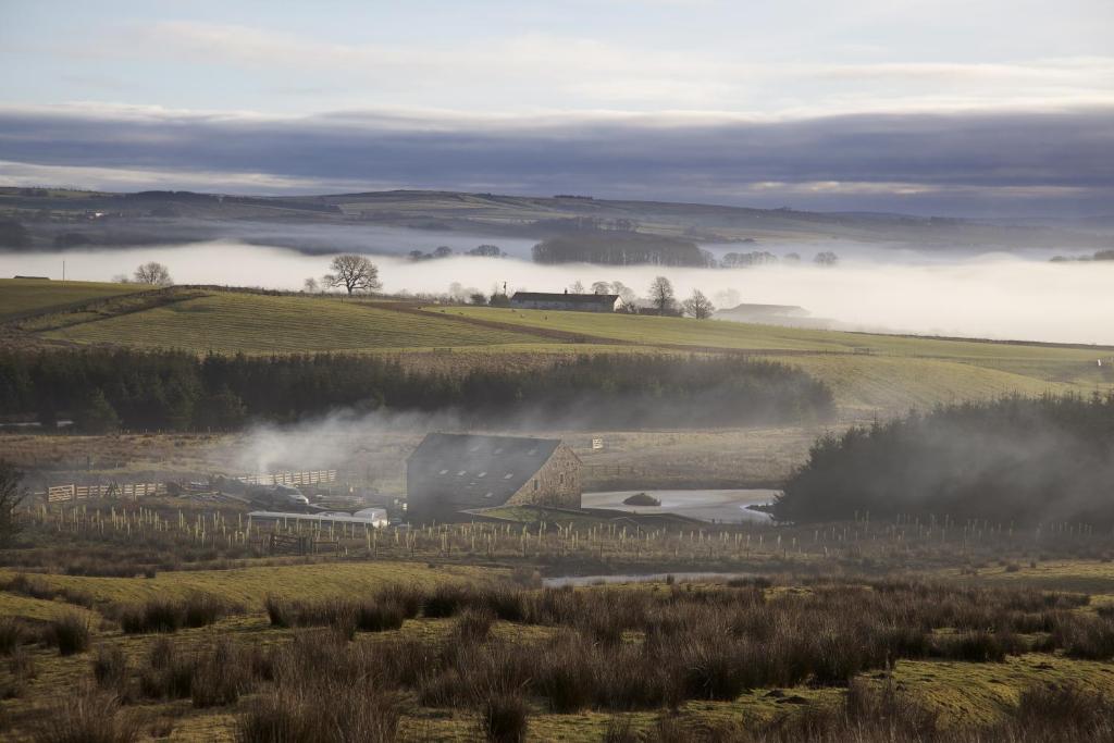a farm in the middle of a field with fog in the background at Laythams Holiday Lets Retreat in Slaidburn