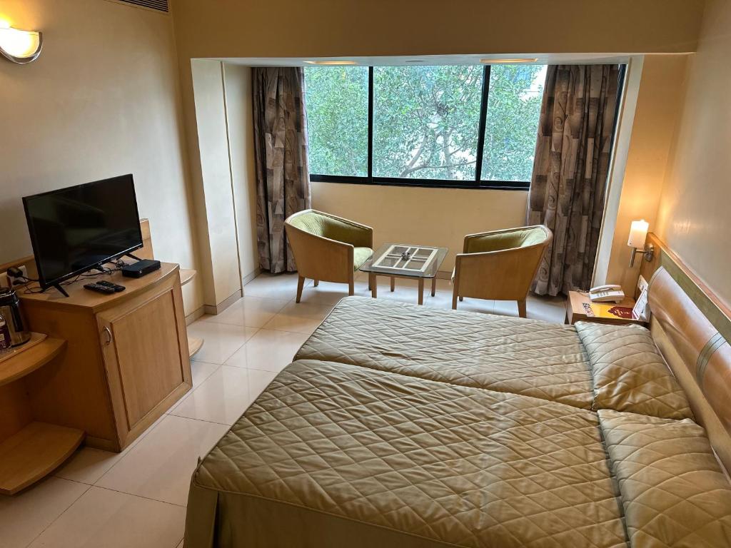 a hotel room with a bed and a desk and a television at Hotel Ashirwad in Pune