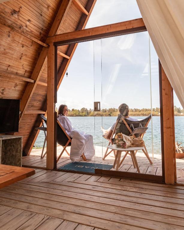 two women sitting in chairs on a deck with a view of the water at Nabi Resort Glamping & SPA in Castel Volturno