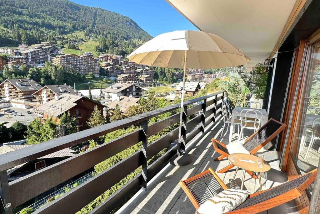 a balcony with a chair and an umbrella at Sunny mountain view apartment in town by Jolidi in Nendaz