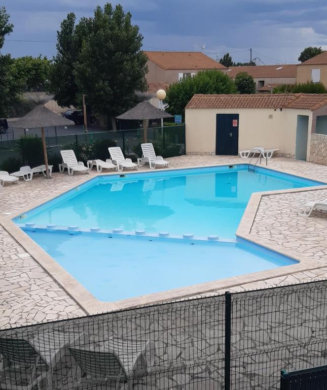 une grande piscine bleue avec des chaises et des tables dans l'établissement Appartement T2, terrasse, piscine, clim, proche plage, à Marseillan