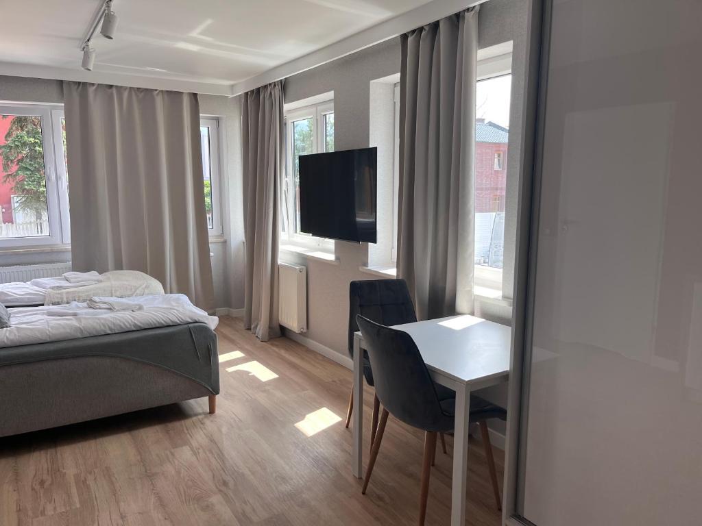 Bright bedroom corner with wall-mounted TV, small desk and twin beds near windows.