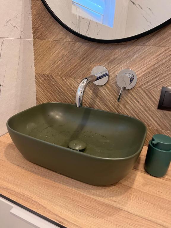 Olive green rectangular basin on wooden countertop beneath round mirror, wall-mounted faucet.