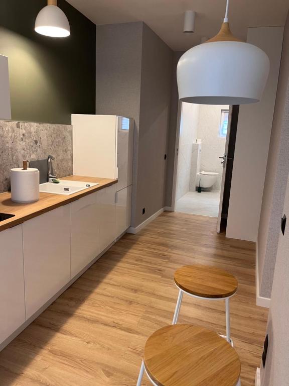 Narrow modern kitchenette with wooden countertops, two round stools, pendant lights, and bathroom doorway.