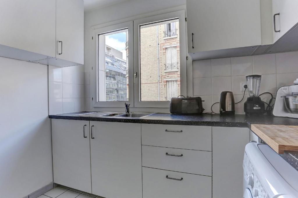 a white kitchen with a sink and a window at Le Charlemagne- Boulogne in Boulogne-Billancourt