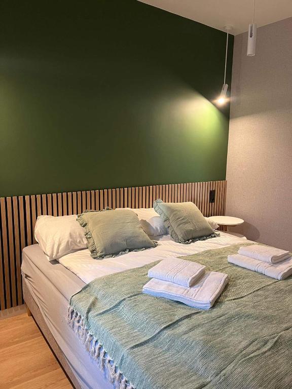 Double bed against green accent wall, wood slatted headboard and neatly folded towels.