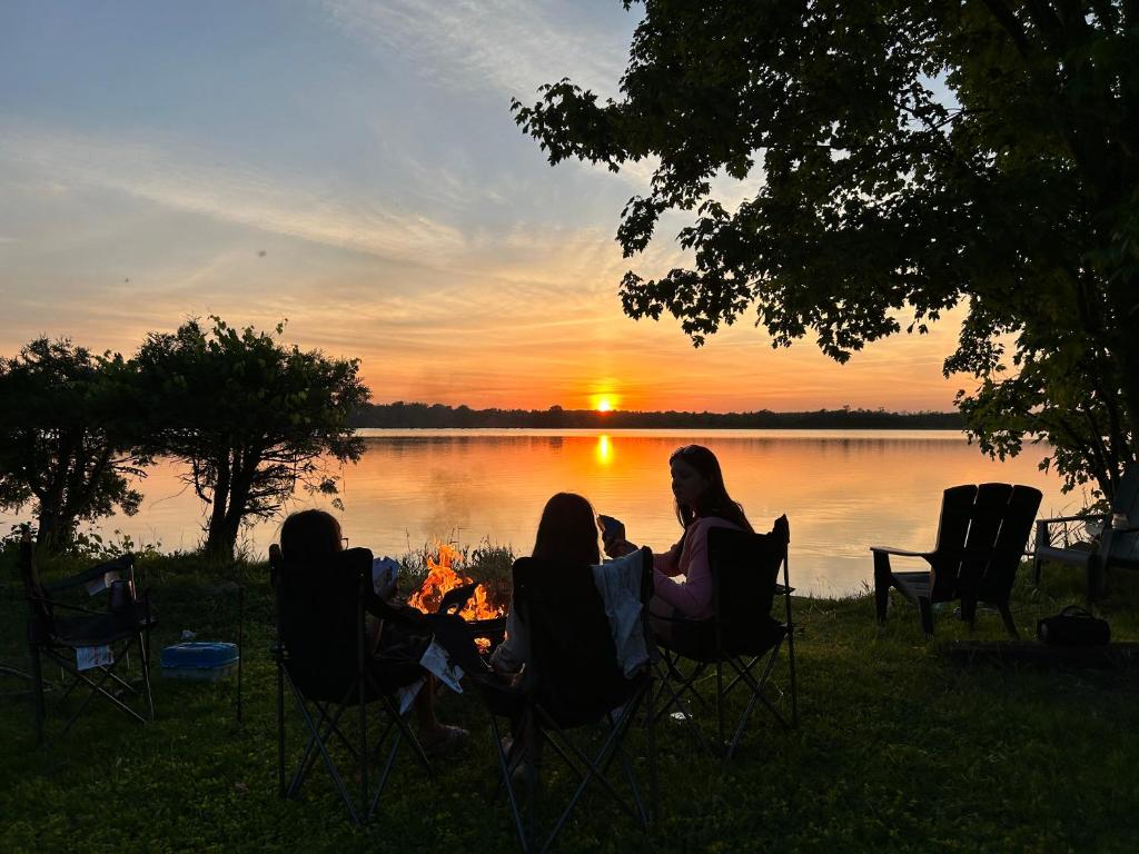 a group of people sitting around a campfire watching the sunset at Modern, Sunset Waterfront Cottage with EV Charger in Yarker