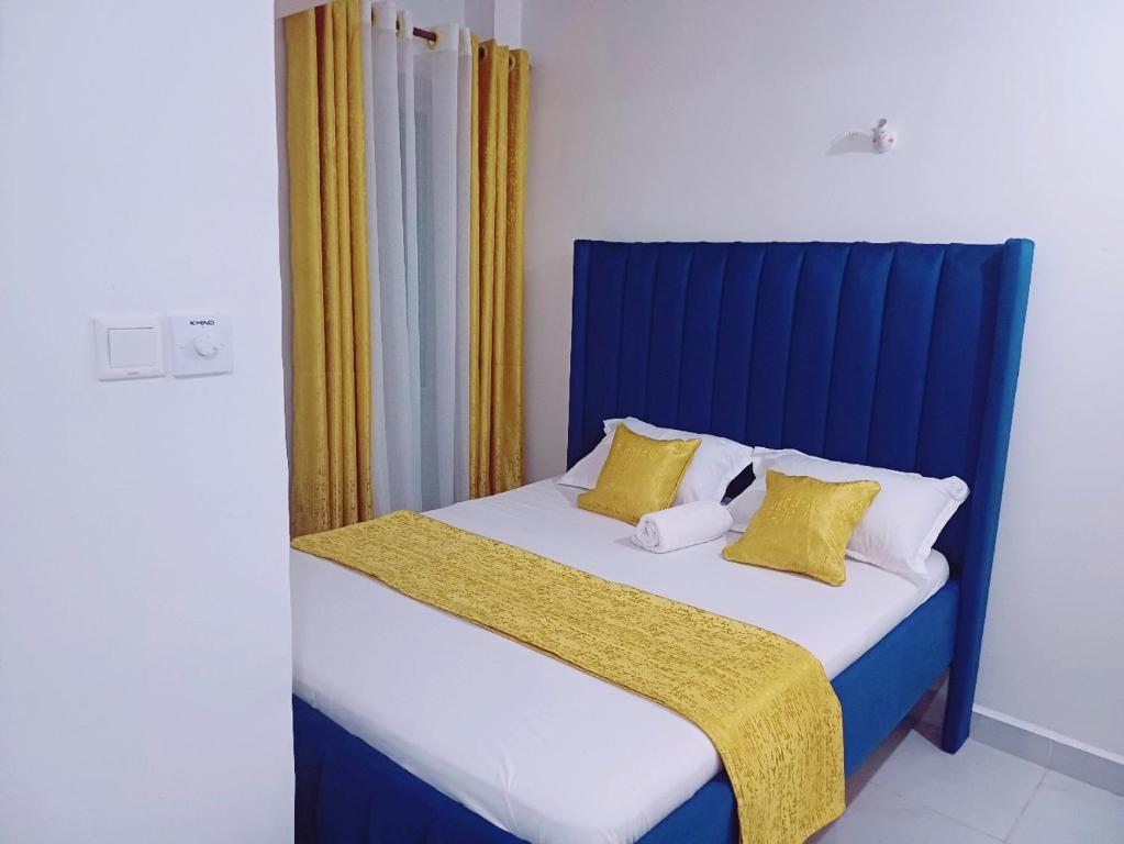a bed with a blue headboard and yellow curtains at Medzam Homes Spacious Newly Furnished Studio in Mombasa
