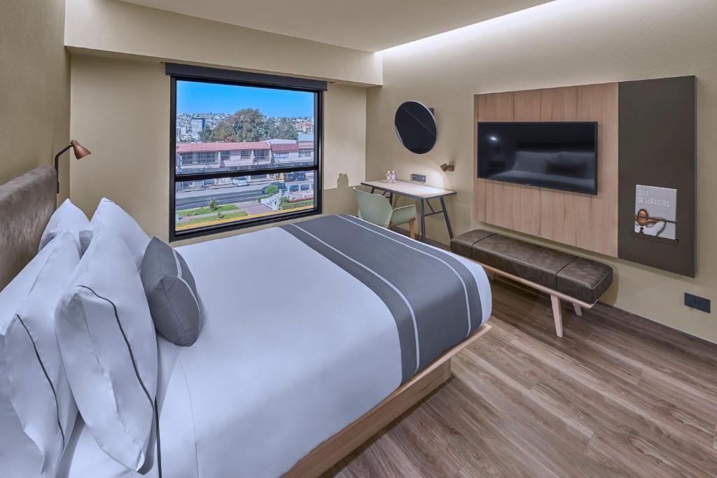 um quarto de hotel com uma cama grande e uma janela grande em City Express Plus by Marriott Tijuana em Tijuana