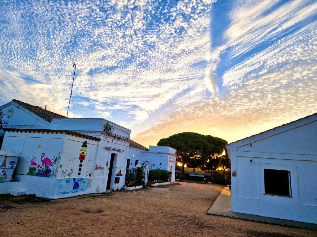 a cloudy sky above two white buildings with the sunset in the background at Albergue Rural Territorio del Gato in El Rompido