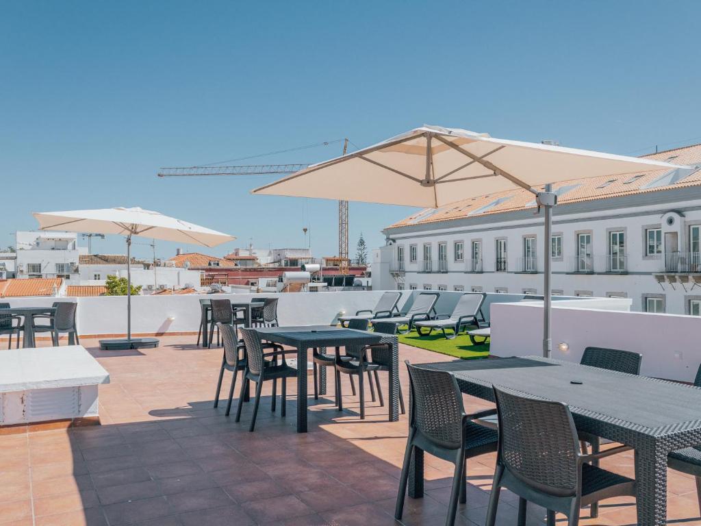 eine Terrasse mit Tischen, Stühlen und Sonnenschirmen auf dem Dach in der Unterkunft Dear Faro - Guest House in Faro