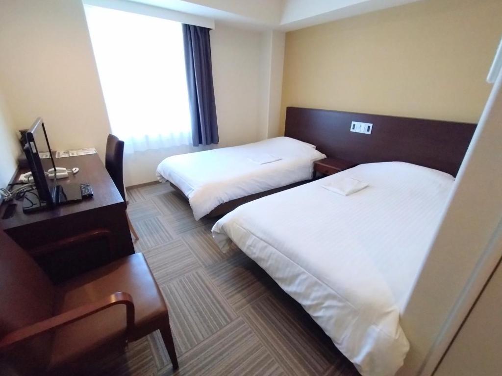 ein Hotelzimmer mit 2 Betten, einem Schreibtisch und einem Fenster in der Unterkunft New Matto Terminal Hotel - Vacation STAY 01878v in Hakusan
