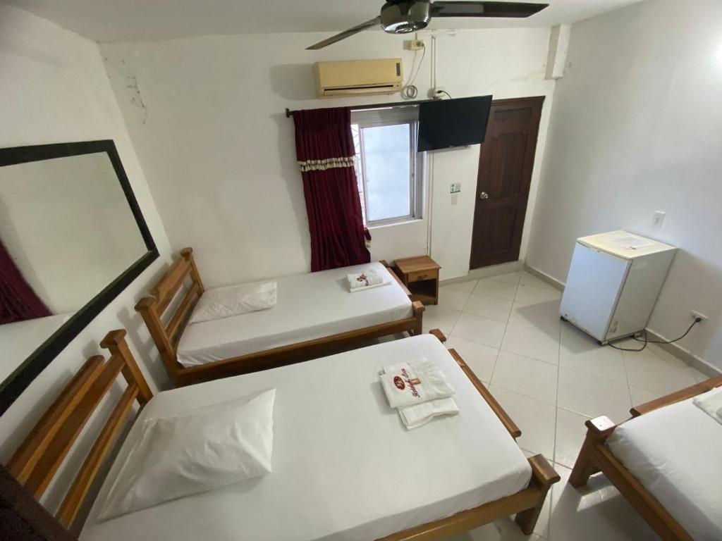 Habitación pequeña con 2 camas y nevera. en Hotel Malecon Puerto Berrio, en Puerto Berrío
