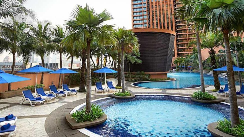 uma piscina com cadeiras e palmeiras e um edifício em Times Square Service Apartment , Kuala Lumpur em Kuala Lumpur