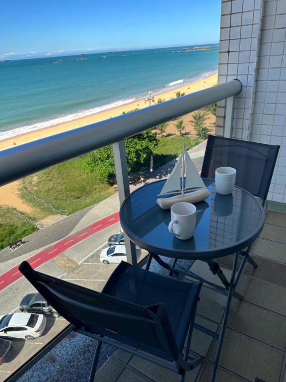 una mesa con 2 sillas y un barco modelo en el balcón en Apartamento Renovado na beira da Praia en Vila Velha