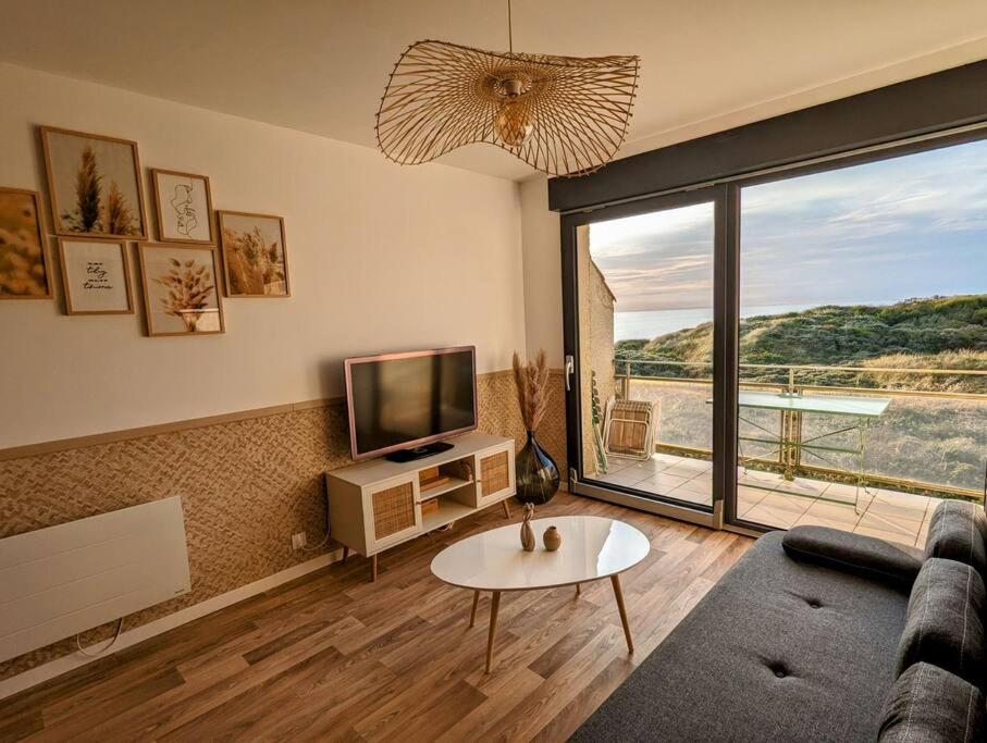 een woonkamer met een bank en een tv bij Duplex au calme avec vue sur les dunes et la mer in Ambleteuse