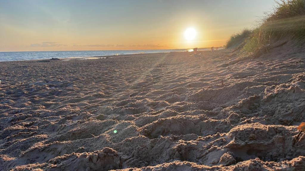 una playa de arena con el sol saliendo sobre el océano en Domek holenderski -noclegi, en Mielno