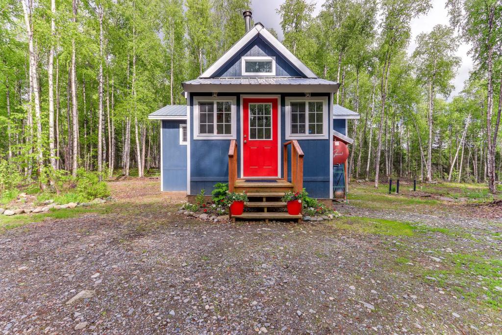 ein winziges Haus mit einer roten Tür im Wald in der Unterkunft Charming Alaska Vacation Rental with Gas Grill! in Talkeetna