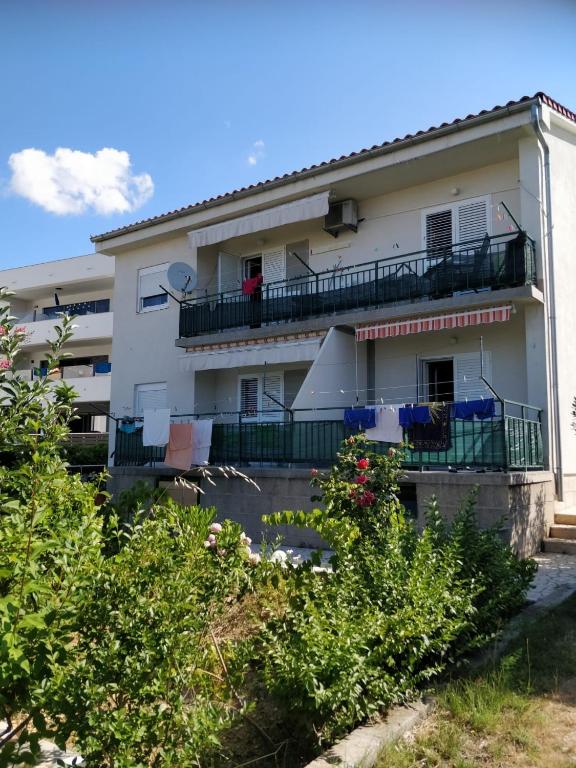 a white building with a balcony and some bushes at Apartment Banjol 4965b in Rab