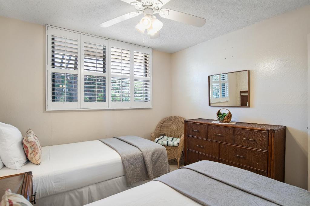 a bedroom with two beds and a dresser and two windows at Kanai A Nalu 214 in Wailuku