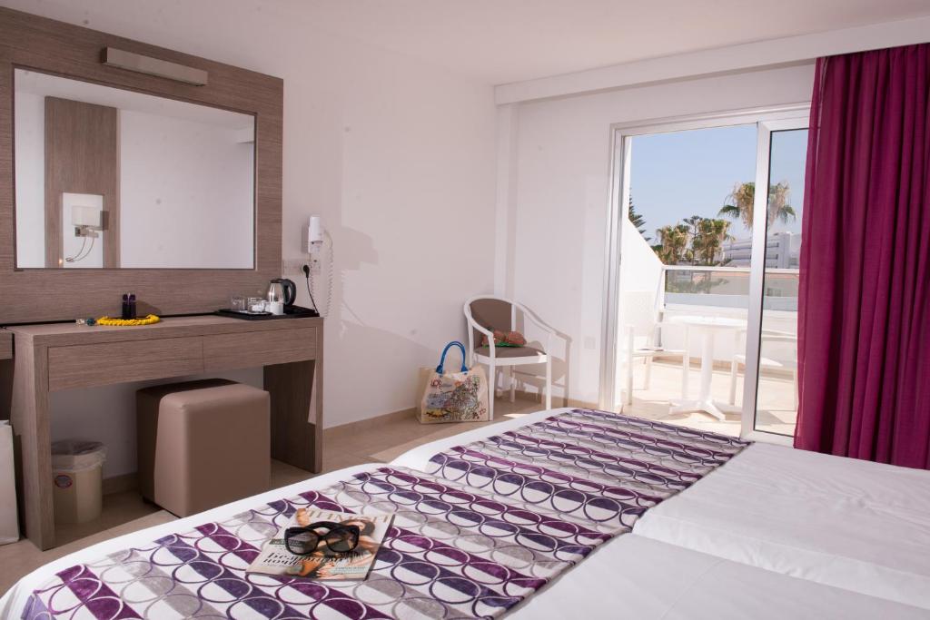 a bedroom with a bed and a desk and a window at New Famagusta Hotel & Suites in Ayia Napa