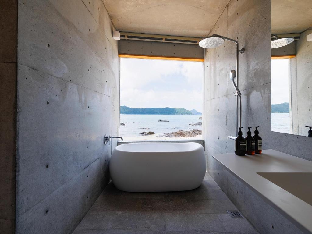 a bathroom with a tub and a large window at Denpaku The Beachfront MIJORA in Amami