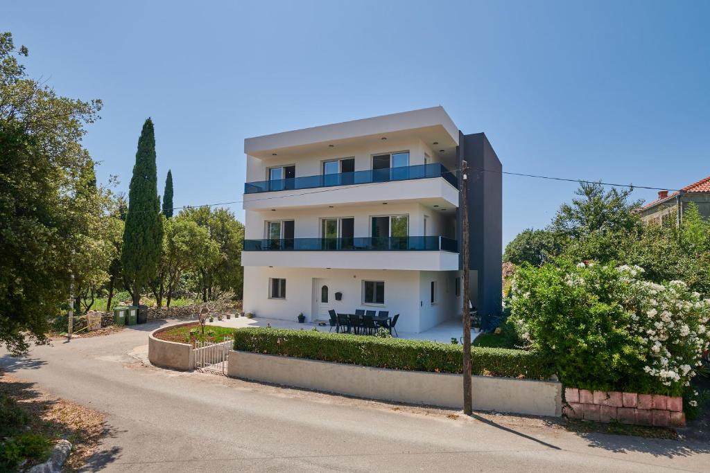 a white house with blue balconies on a street at Apartments Endji in Čilipi