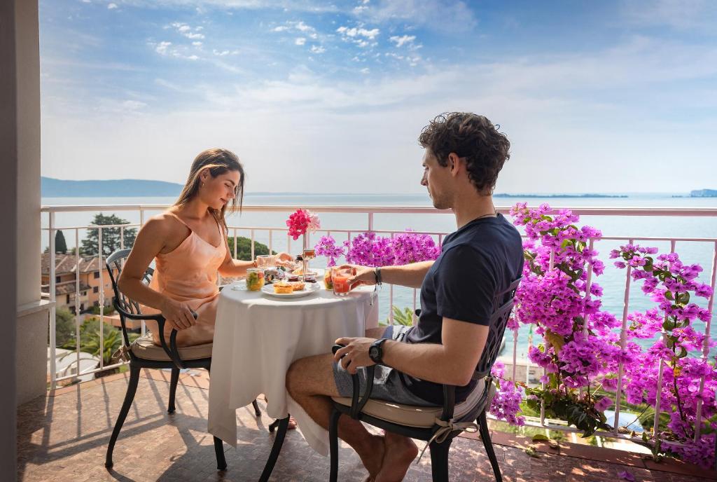 Ein Mann und eine Frau, die an einem Tisch auf einem Balkon sitzen in der Unterkunft Hotel Villa Florida Suites & Suite Apartments in Gardone Riviera