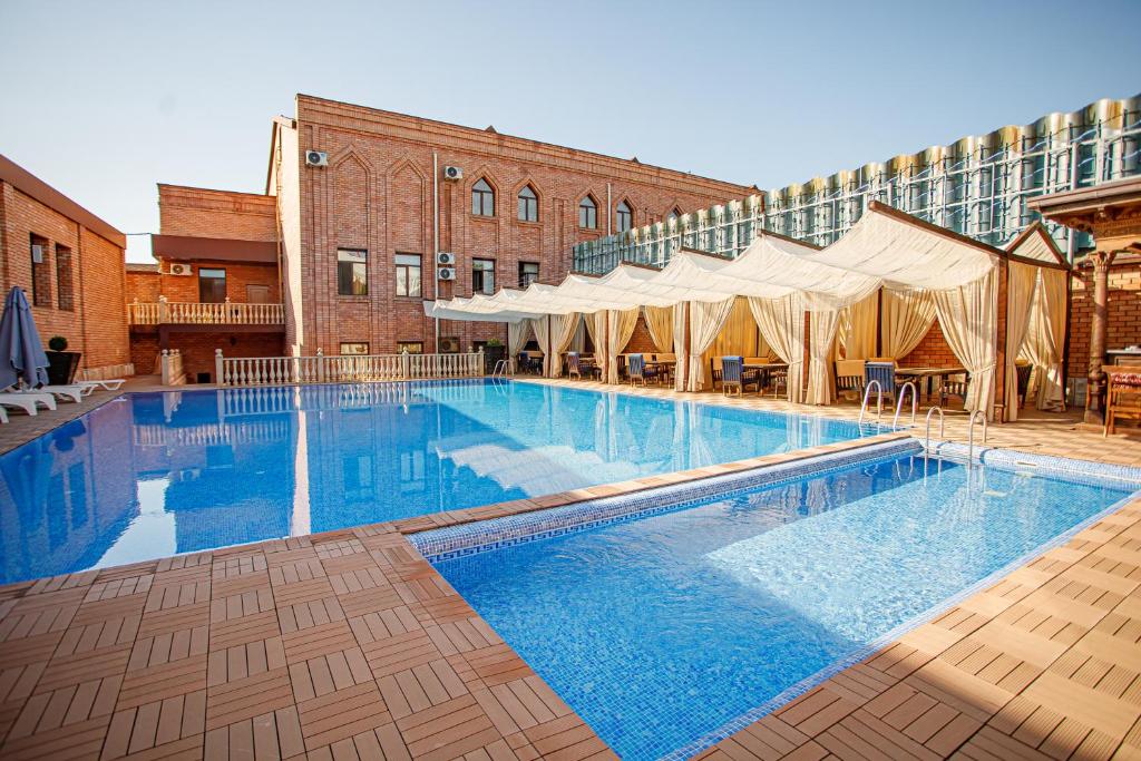 a large swimming pool next to a building with tents at Ichan Qal'a Premium Class Hotel in Tashkent