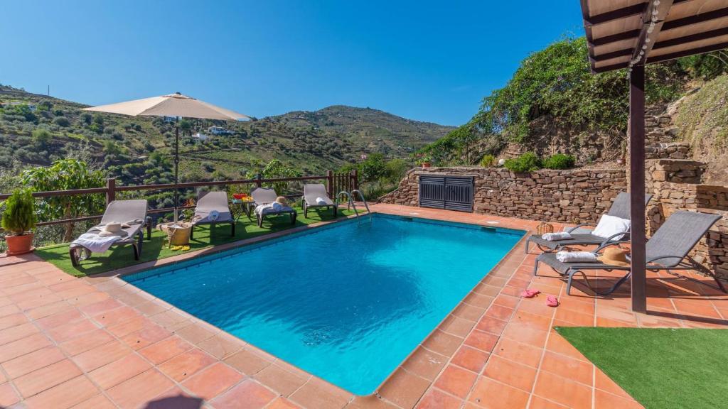 een zwembad met stoelen en een berg op de achtergrond bij Casa Amelia Competa by Ruralidays in Cómpeta