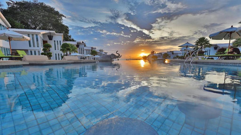a large swimming pool with a sunset in the background at Vannee Golden Sands Beachfront Resort in Haad Rin