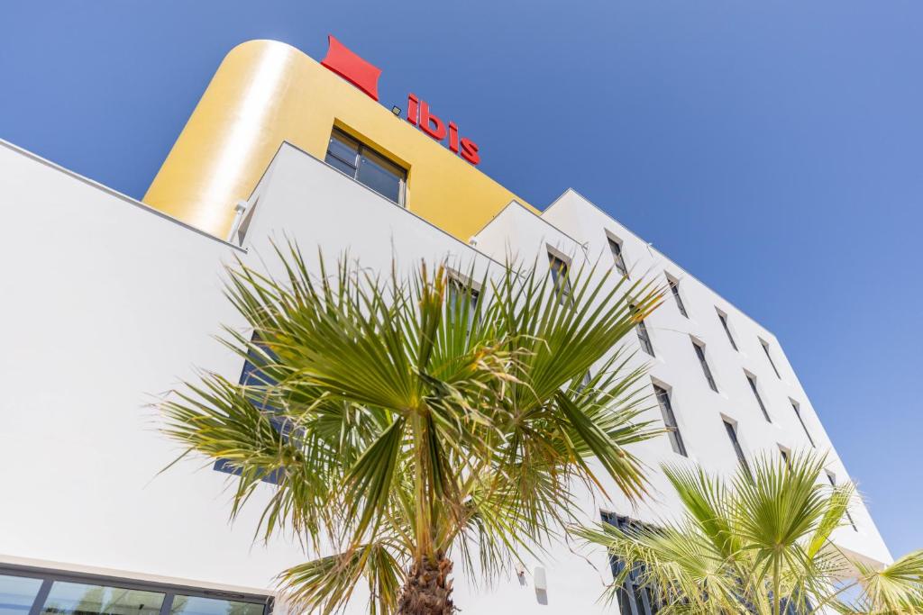 a hotel with palm trees in front of it at Ibis Marseille Marignane Technopole in Marignane