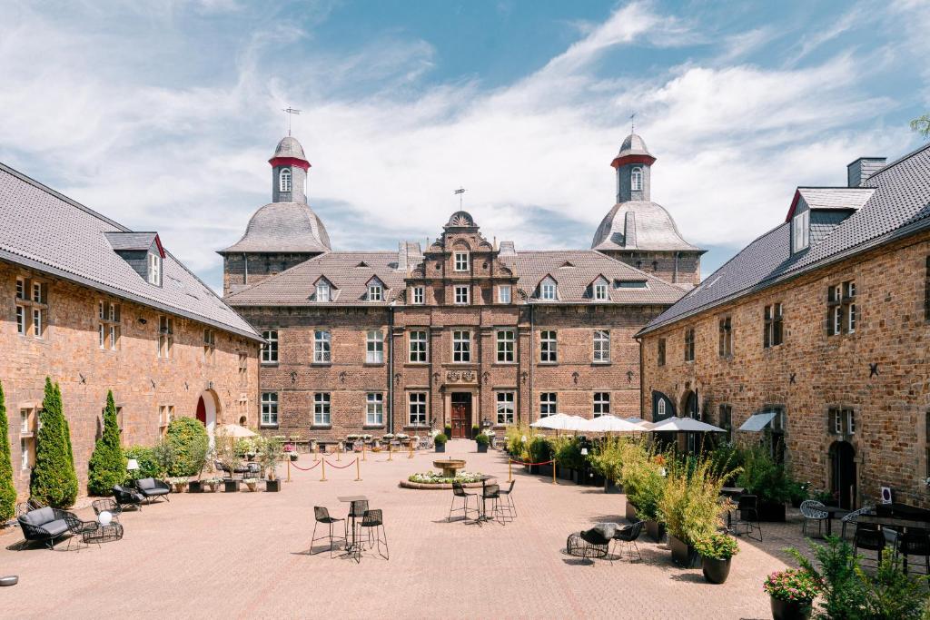 a courtyard in a large brick building with chairs and tables at Schlosshotel Hugenpoet in Essen