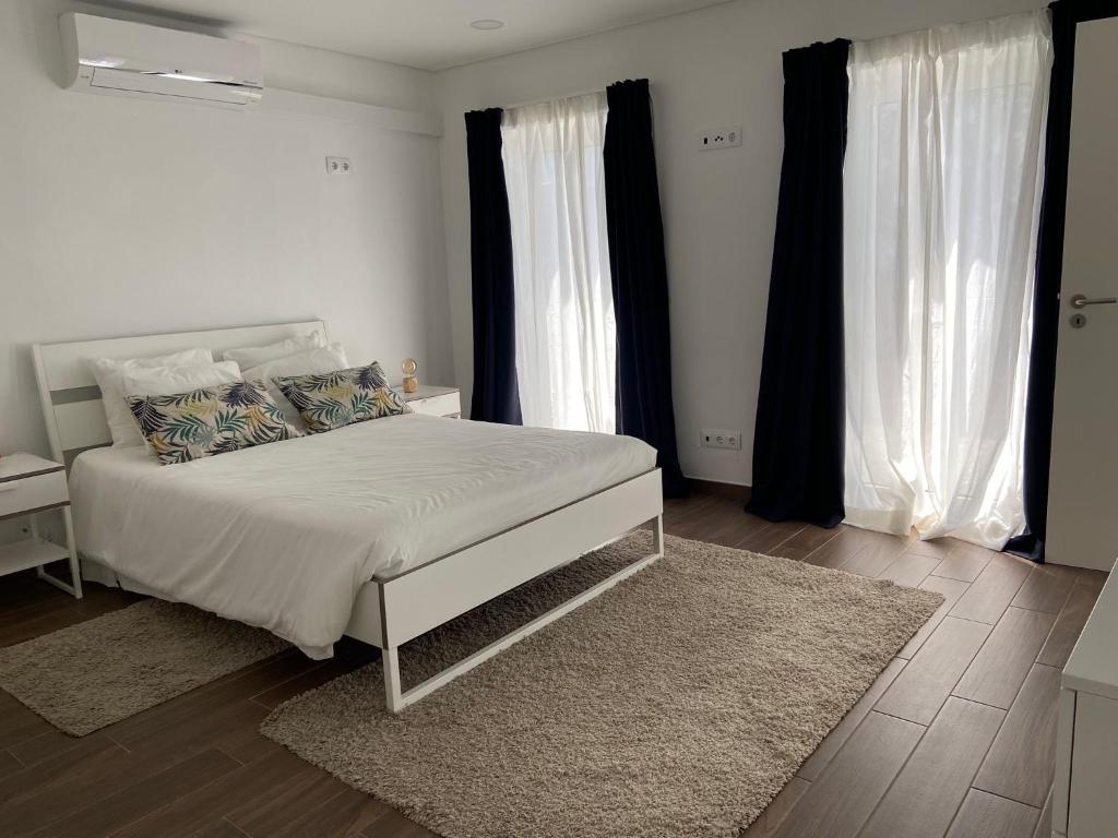 a white bedroom with a white bed and two windows at A Casinha in Angra do Heroísmo