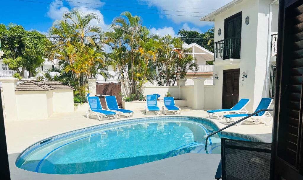 a swimming pool with blue chairs and a house at Mango Crescent in Saint James