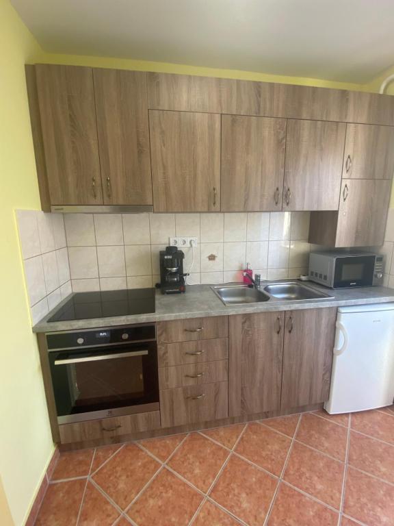 a kitchen with wooden cabinets and a sink and a microwave at Hajnal Vendégház in Hajdúszoboszló