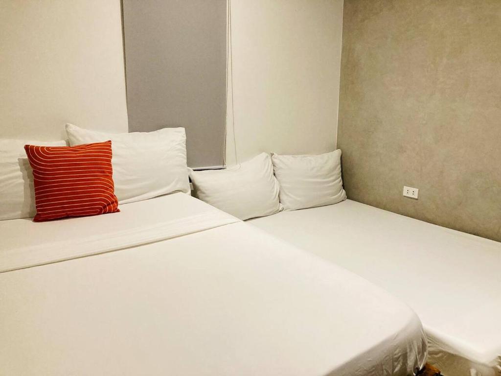 um quarto com 2 camas com lençóis brancos e uma almofada vermelha em Barkada Room 1 near Clark (Casa Isabela) em Mabalacat