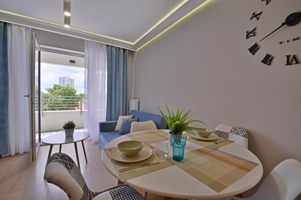 een woonkamer met een tafel en stoelen en een klok bij Apartamenty Bryza - Sun Towers in Świnoujście