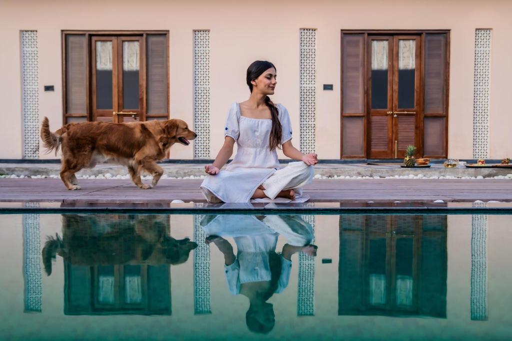 a woman sitting next to a pool with her dog at Parijat Private Pool Villa in Udaipur