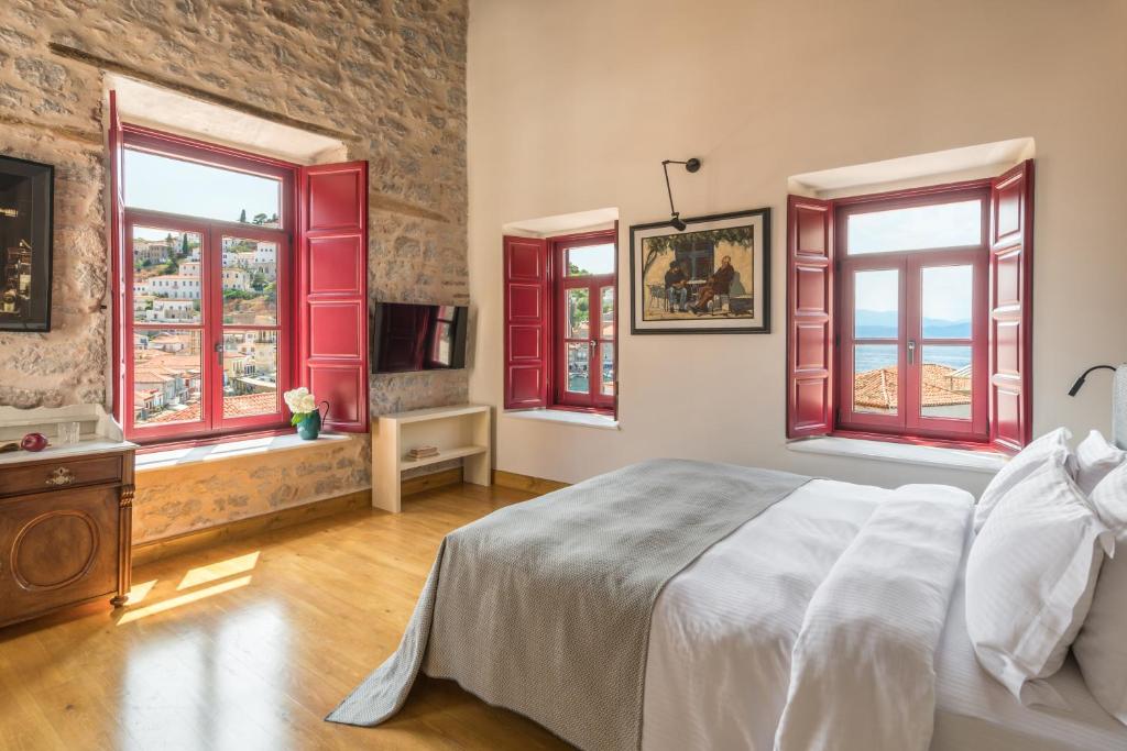 FOS Hydra residence في هيدرا: غرفة نوم بنوافذ حمراء وسرير كبير