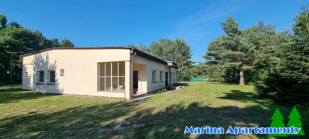 Una pequeña casa blanca en un patio con árboles. en Marina Apartamenty, en Rozewie
