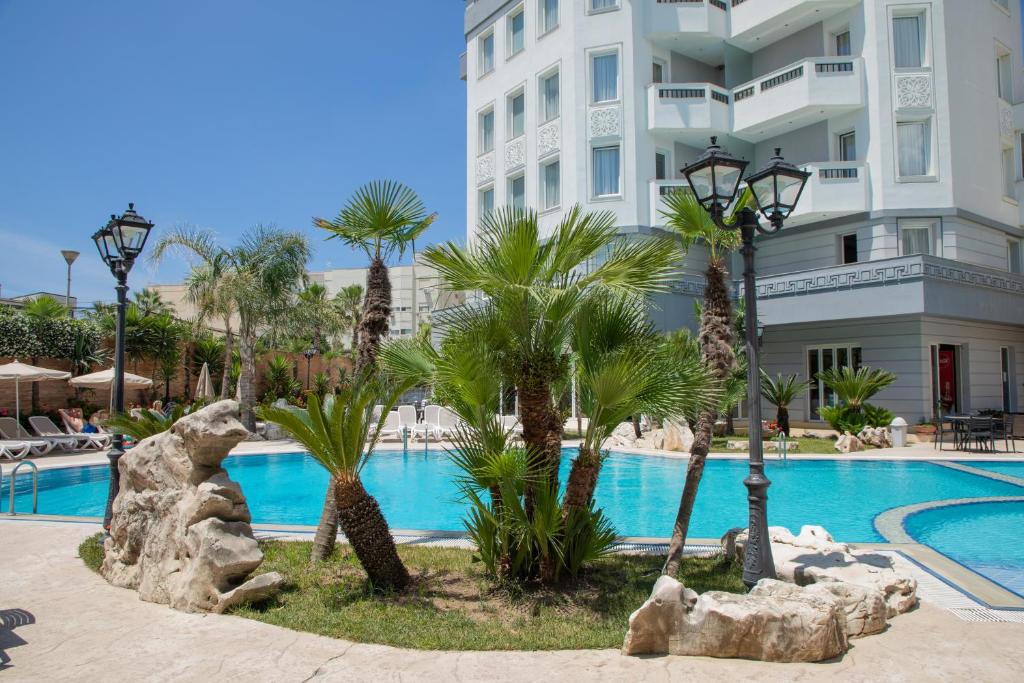 um resort com piscina, palmeiras e um edifício em Hotel Dyrrah em Durrës