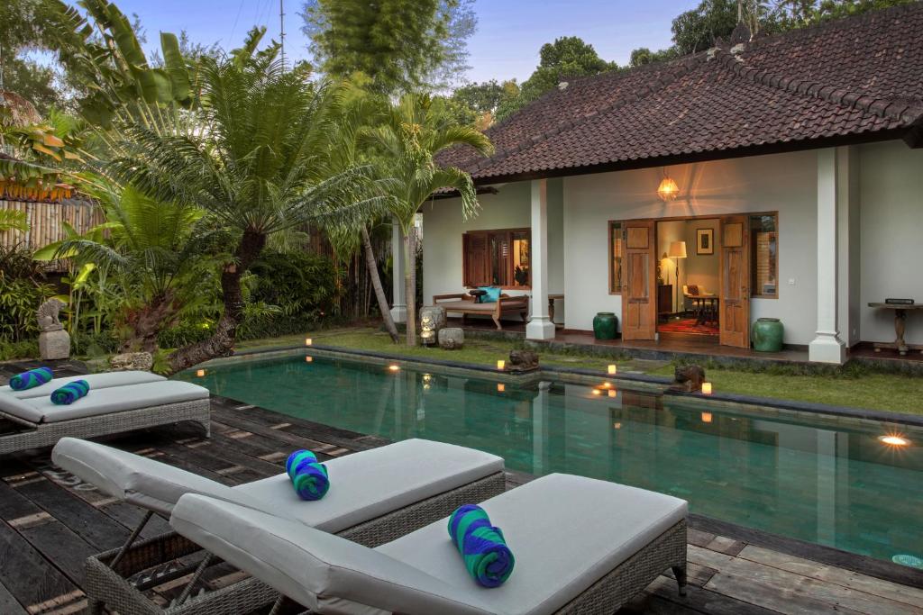a villa with a swimming pool and two lounge chairs at Room & Vespa 3 in Seminyak