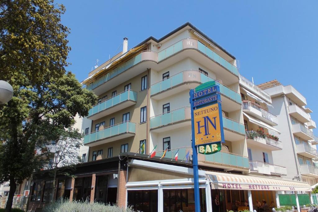 een hoog wit gebouw met een bord ervoor bij Hotel Nettuno in Sottomarina