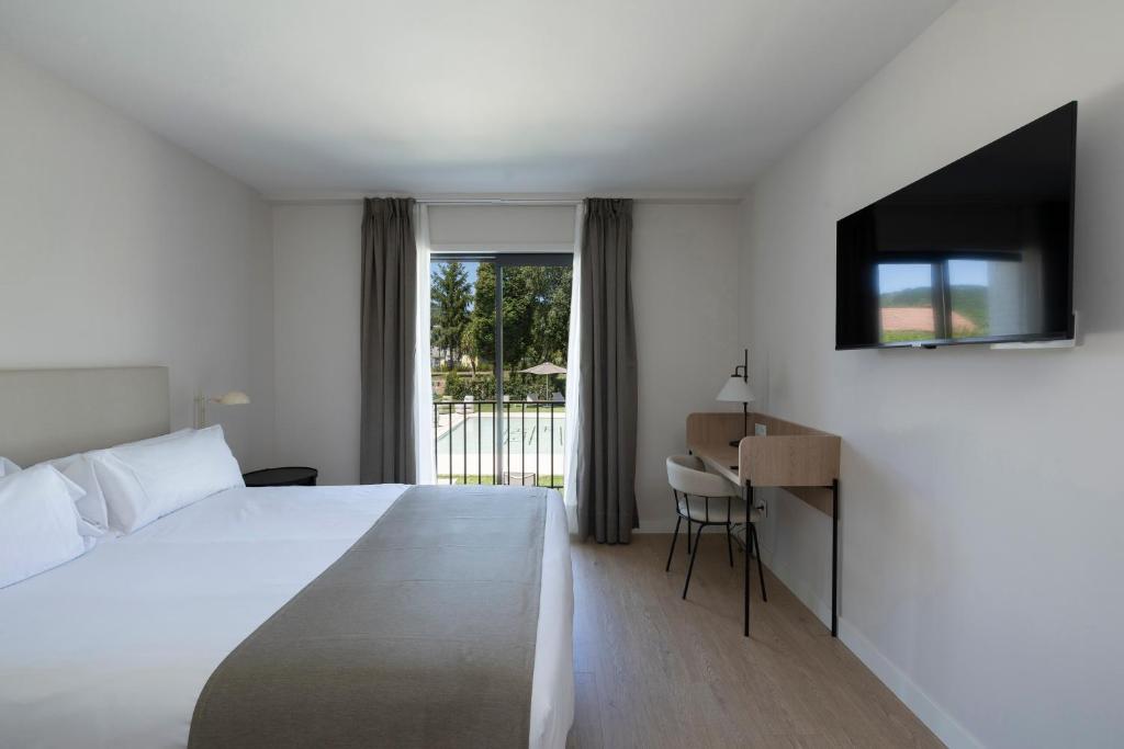 a hotel room with a bed and a desk and a window at Hotel H4 Cangas 3 Superior in Cangas de Morrazo