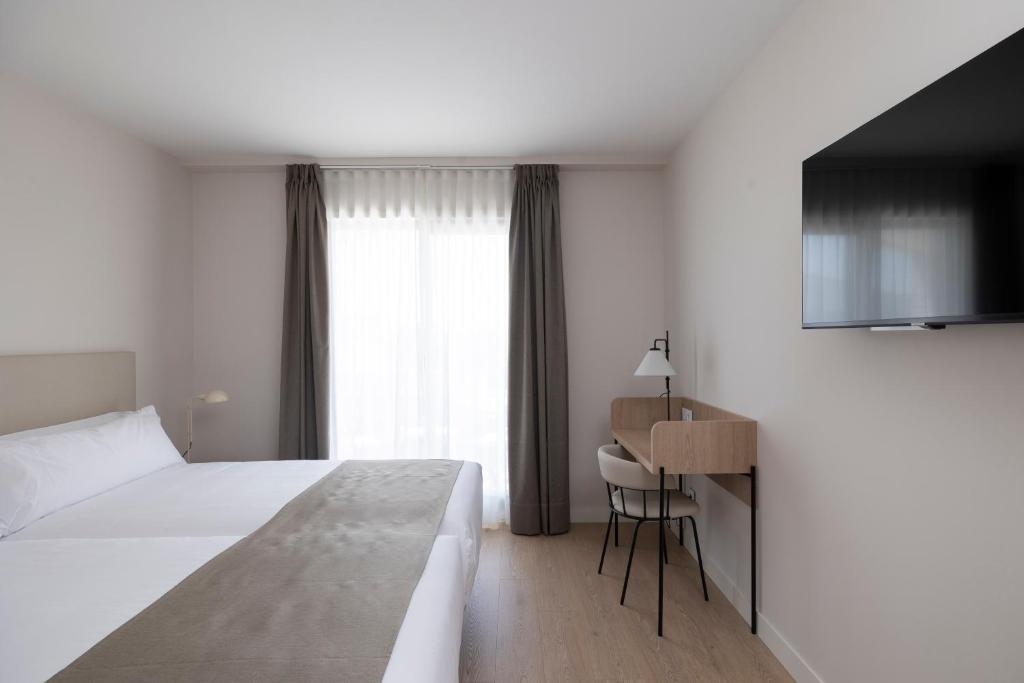 a bedroom with a bed and a desk and a window at Hotel H4 Cangas 3 Superior in Cangas de Morrazo