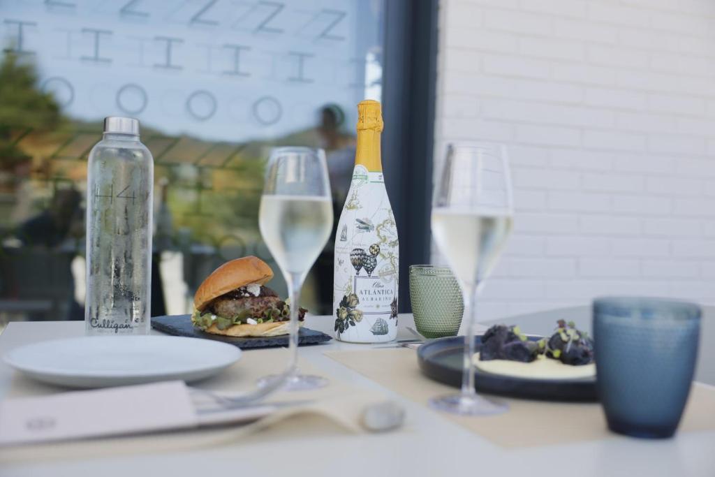 a table with two glasses and a sandwich and wine bottles at Hotel H4 Cangas 3 Superior in Cangas de Morrazo