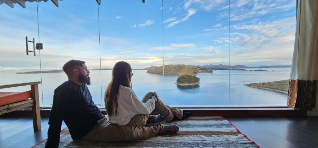 un hombre y una mujer sentados en el suelo frente a una gran ventana en Inti Illimani Lodge en Comunidad Yumani