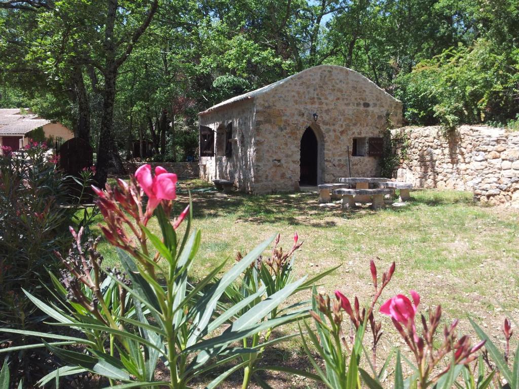 an old stone building in a yard with pink flowers at Le Donjon des Combes et son Spa in Fayence