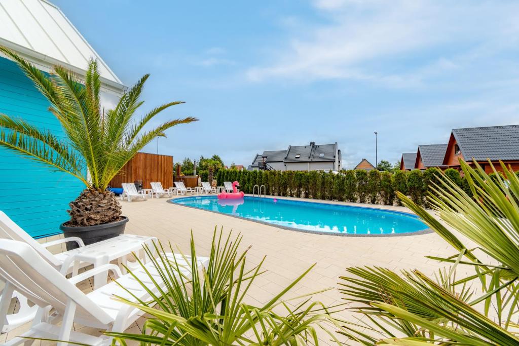 una piscina con sillas blancas y una palmera en Domki Piaskowa11 Palm Resort & Wellness en Łeba